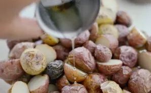 Kai bulvės atvės, perpjaukite jas pusiau. Sudėkite jas į salotų dubenį. Supilkite 1 valg. šaukštą riebalų.