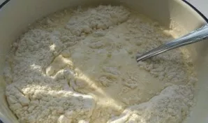 Dalimis išsijokite miltus į kefyrą. Išminkykite nelipnią tešlą.