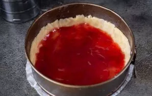 Ant tešlos pagrindo dugno dėkite braškių uogienę ir šaukštu tolygiai paskirstykite ją sluoksniu.
