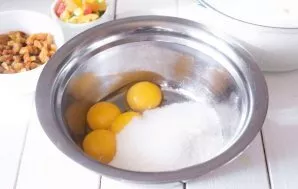 Į dubenį sudėkite trynius ir suberkite visą likusį cukrų. Viską išmaišykite šluotele.